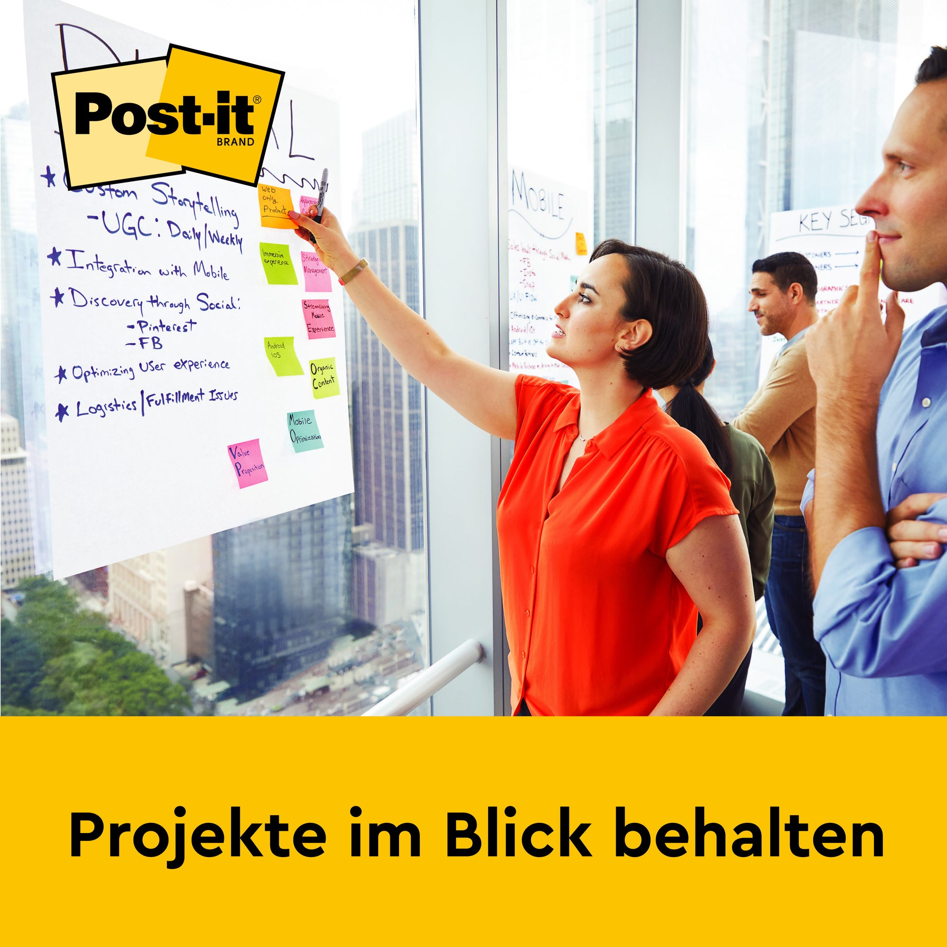 Eine Frau schreibt auf große Post-it® Super Sticky selbsthaftendes Recycling Meeting Chart Blätter, die an ein Fenster geklebt sind, während drei andere zusehen. Der Text lautet: "Projekte im Blick behalten". Das Post-it Logo der 3M Deutschland GmbH erscheint in der oberen linken Ecke.
