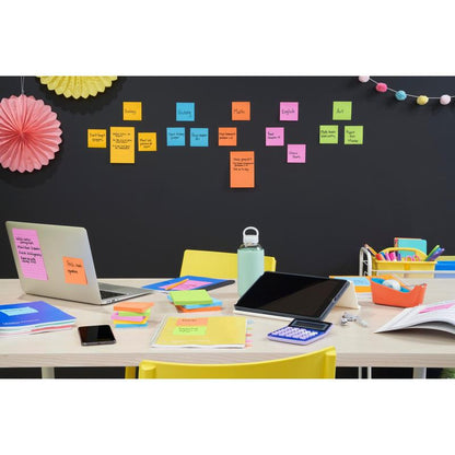Stôl s laptopom, tabletom, kalkulačkou, telefónom, fľašou vody a farebnými kancelárskymi potrebami. Za nimi Post-it® Super Sticky Notes (76x127mm) od 3M Deutschland GmbH usporiadajú školské predmety na stene, nad nimi visia dekorácie.