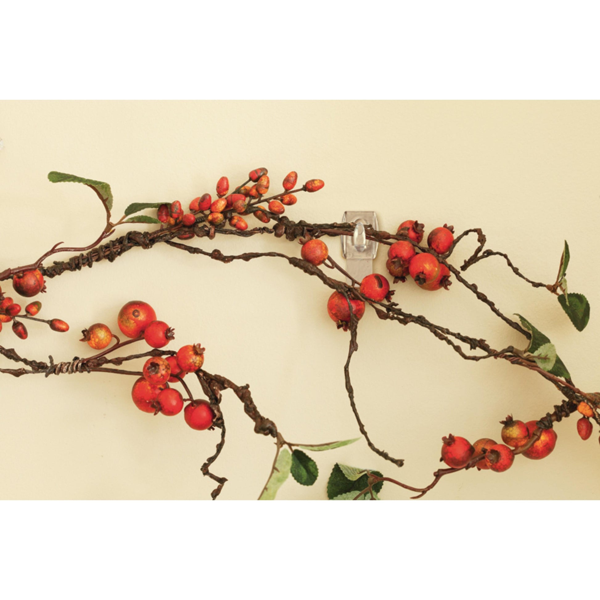 Eine Nahaufnahme von ineinander verschlungenen Zweigen mit roten Beeren und grünen Blättern, die mit einem transparenten Command™ Mini-Haken (17006CLR, 1 Stück) der 3M Deutschland GmbH an einer Lichtwand befestigt wurden.