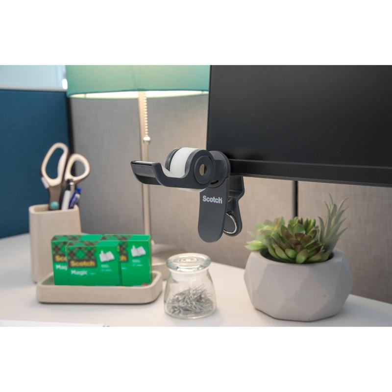 Na stole: lepiaca páska 3M Scotch™ Clip & Twist s neviditeľnou páskou Scotch® Magic™ (19 mm × 8,89 m), lampa, nožnice v držiaku, dve ďalšie rolky lepiacej pásky Scotch®, pohár so špendlíkmi a malá sukulentná rastlina v kvetináči.
