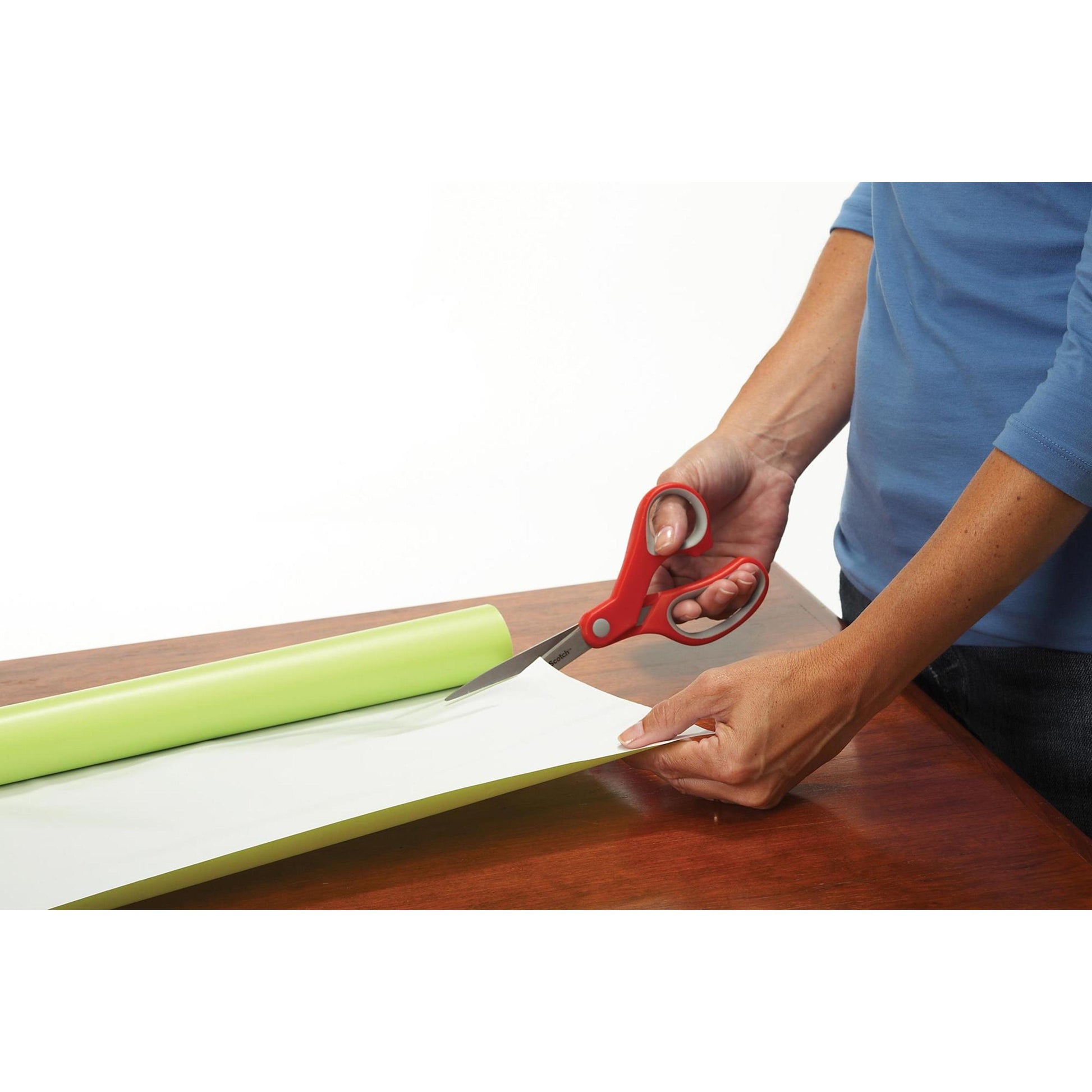 Eine Person im blauen Hemd benutzt die Scotch™ Präzisionsschere rot von 3M Deutschland GmbH, um teilweise abgerolltes hellgrünes Papier oder Vinyl auf einer Holzoberfläche zu schneiden.