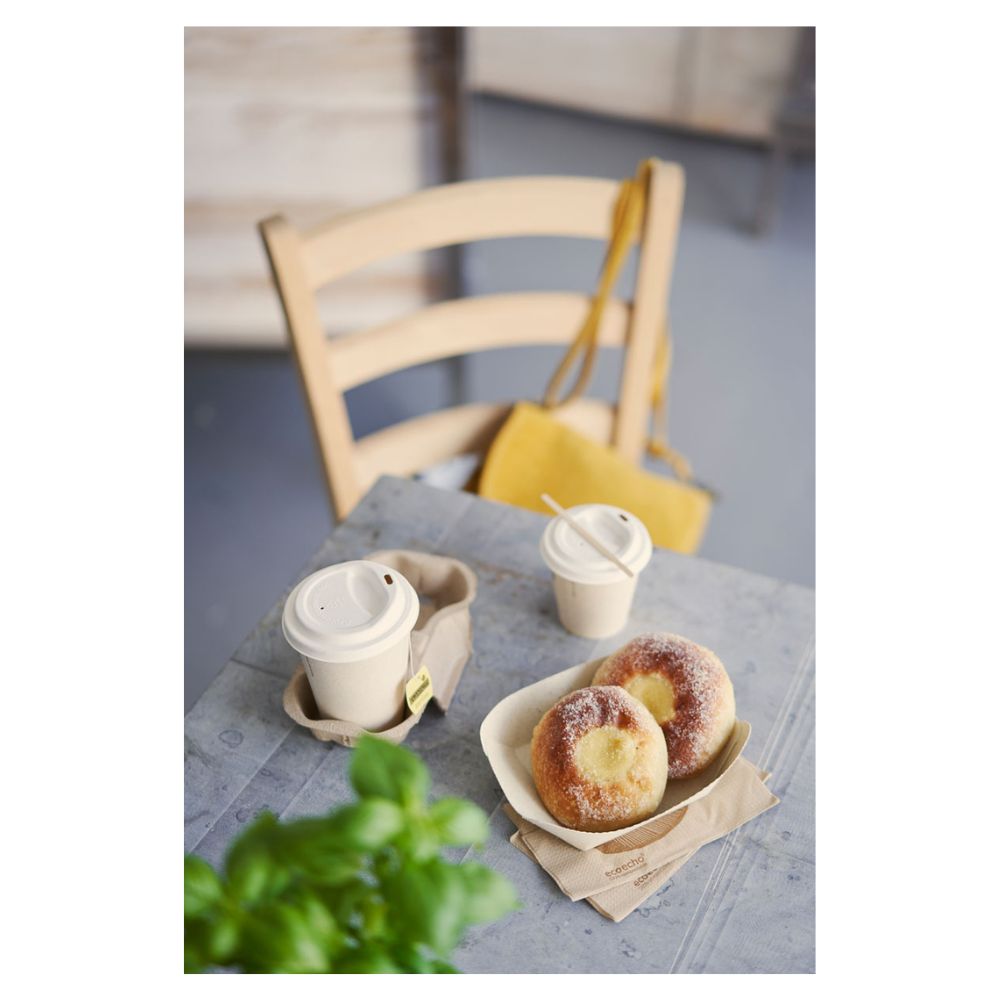 Na stole ležia dva cukrom posypané pečivá na podnose a dva s vrchnákom vybavené Duni kávové poháre „Sweet Tlačená Bagasa“ od Duni GmbH. Žltá kabelka visí na drevenej stoličke, zatiaľ čo čiastočne viditeľná zelená rastlina v popredí zvýrazňuje jemnú tému udržateľnosti.